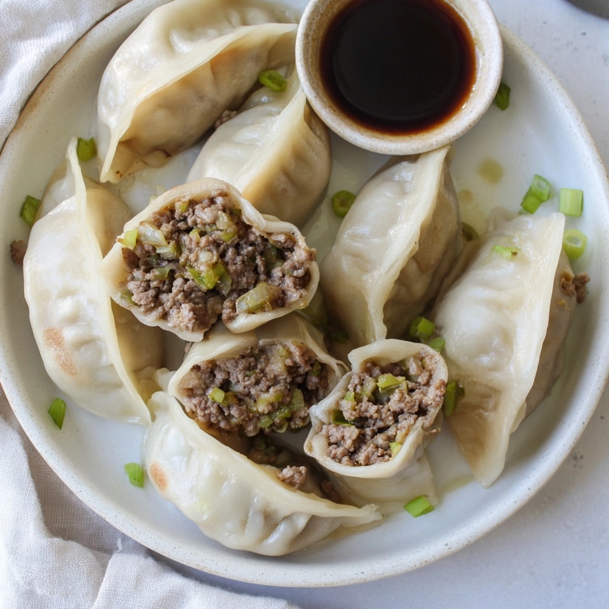 Close-up of pan-fried Beef Shiitake Dumplings, golden brown and crispy, served with sauce.