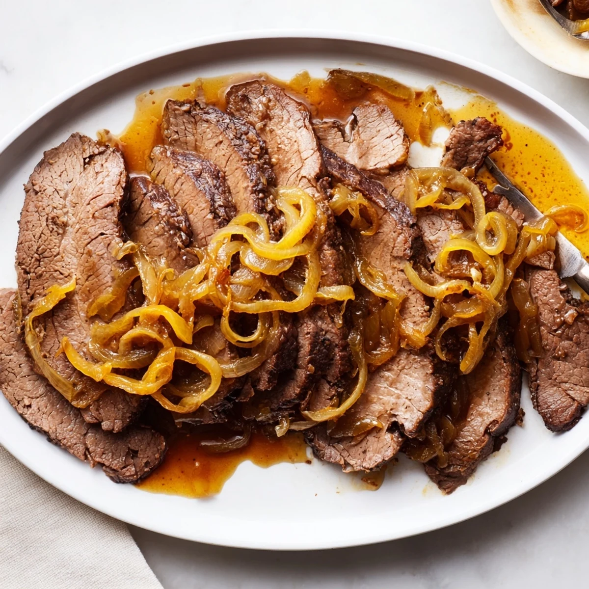 A close-up shows juicy slices of slow cooked beef brisket with savory onions and flavorful pan juices.