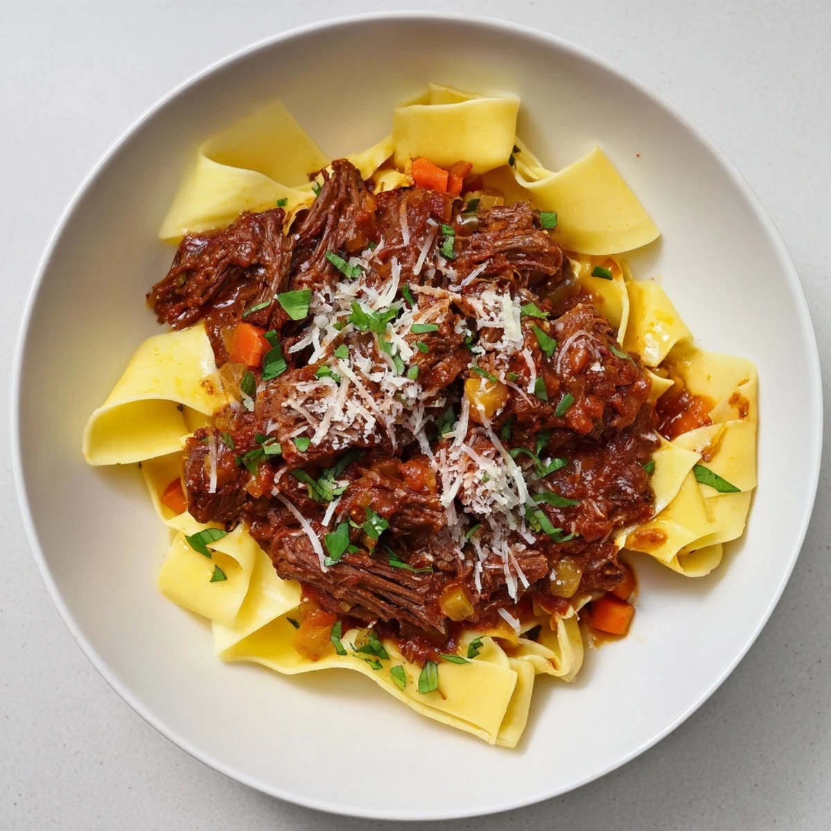Creamy parmesan topping on slow cooked beef ragu with pappardelle, highlighting a comforting Italian meal.