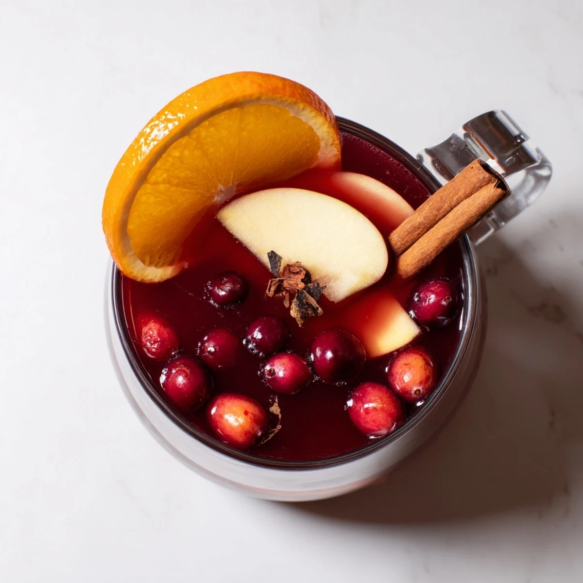 Bright red Spiced Holiday Punch with floating apple and orange slices, ready to serve warm.