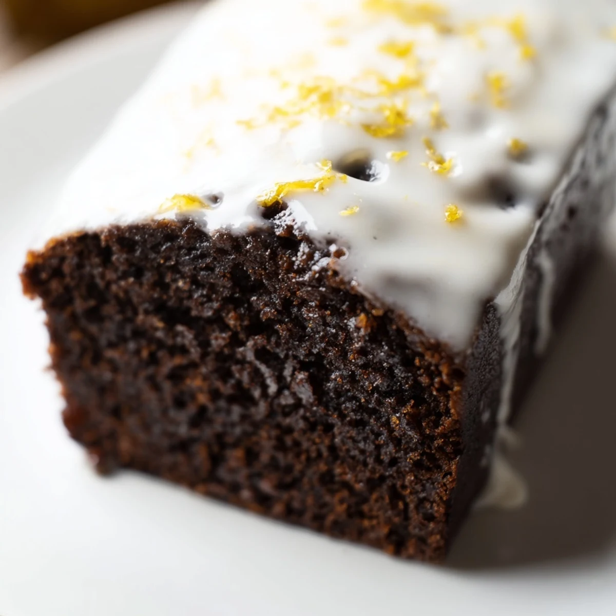 Overhead view of Gingerbread Loaf with Lemon Cream Cheese Glaze garnished with fresh lemon zest and a sprig of rosemary.