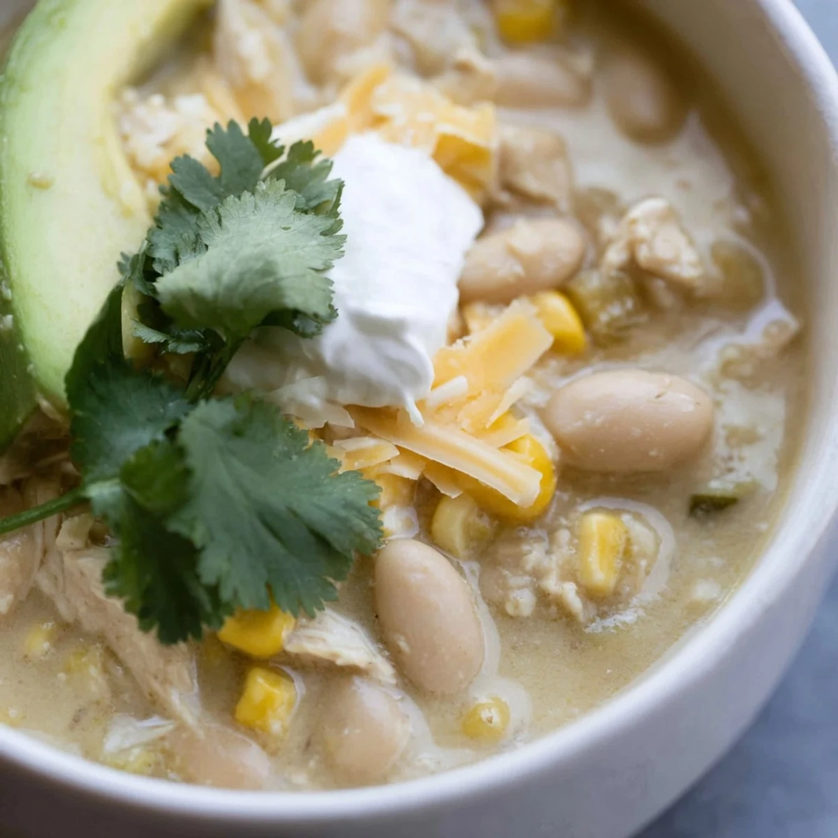 White Chicken Chili with Corn and Beans ladled into a rustic bowl, topped with fresh cilantro and avocado slices.