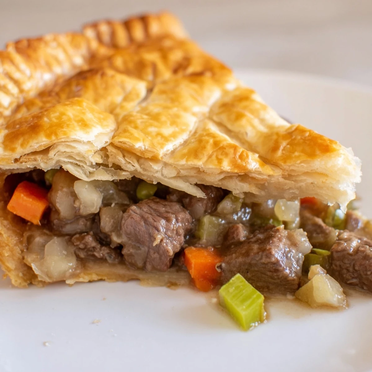 A slice of Beef Pie with Crust rests on a white plate, served alongside creamy mashed potatoes and bright green beans.