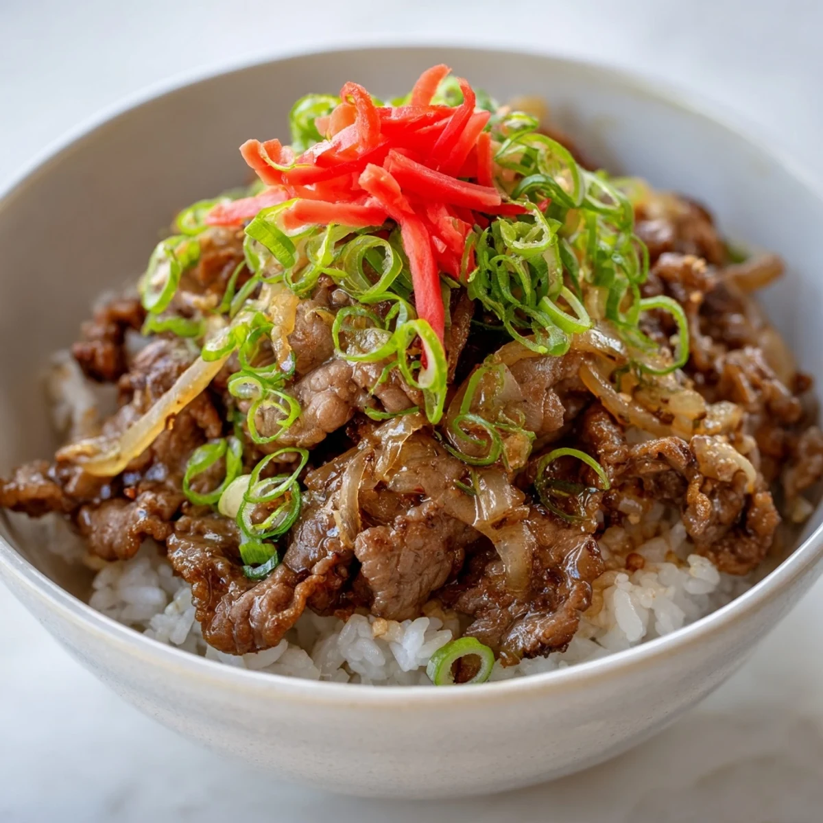 Savory beef and onion sauté simmered in a sweet soy glaze, piled high on fluffy steamed rice in a warm bowl.