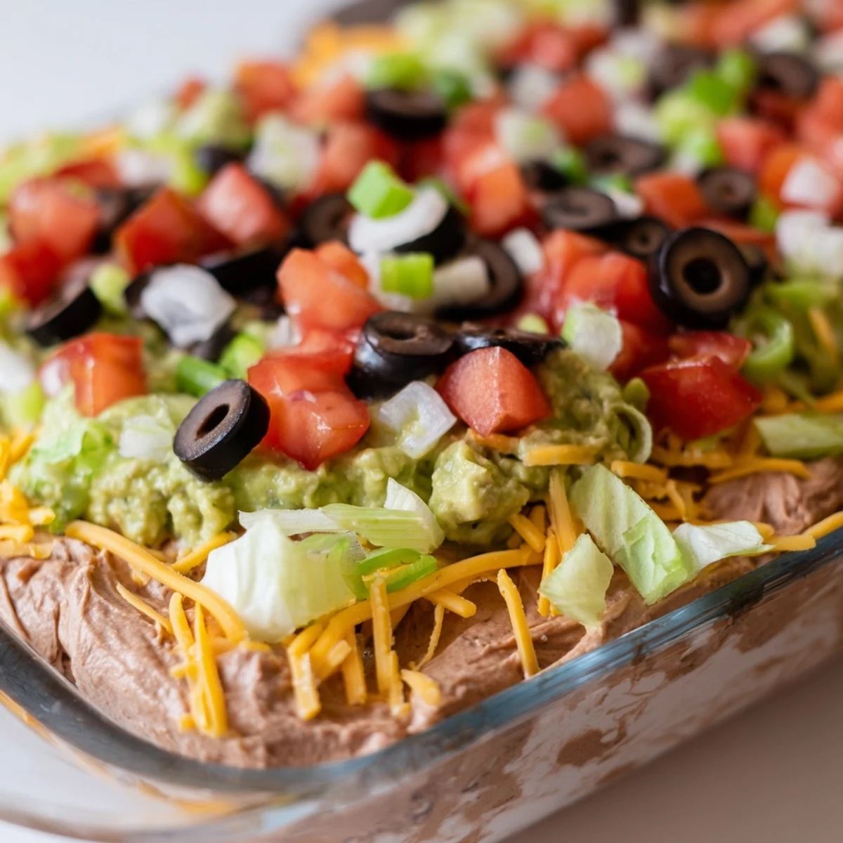 Chilled Tex-Mex Super Bowl Seven Layer Taco Dip topped with fresh lettuce, tomatoes, and black olives, ready for a game day crowd.