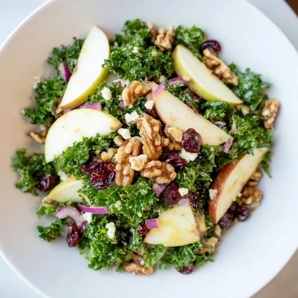 Green Kale and Apple Salad with Walnuts glistening with maple-Dijon dressing in a white bowl.