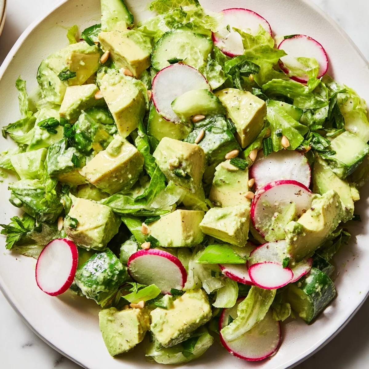 Overhead view of the salad, highlighting the creamy green goddess dressing coating romaine lettuce, cucumber, and avocado, garnished with sunflower seeds for crunch.