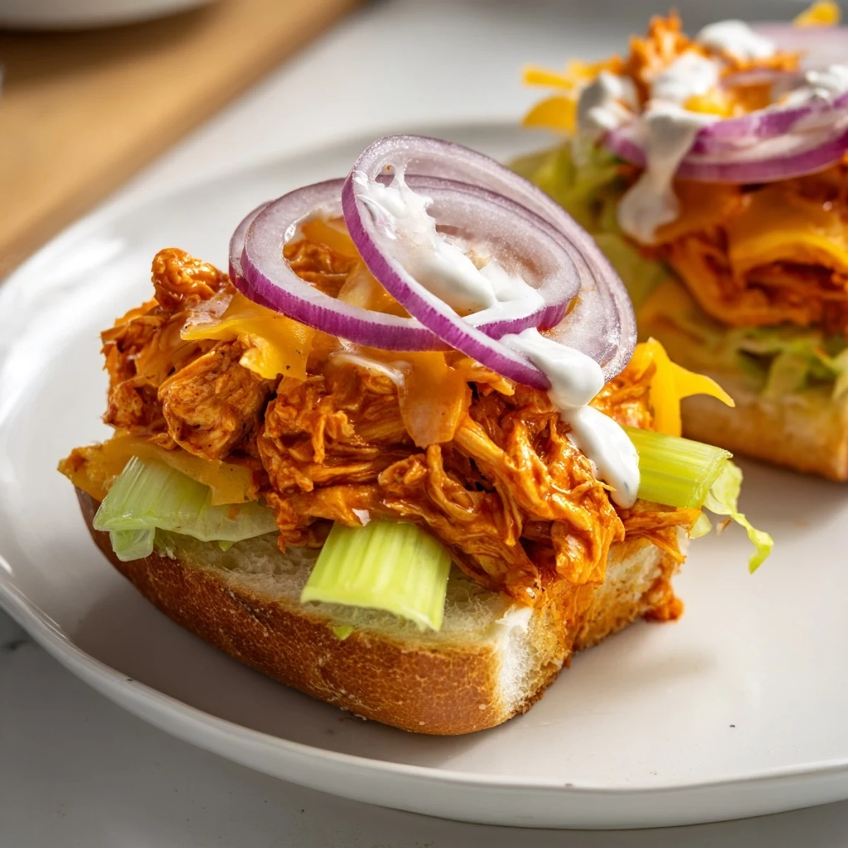 Warm Buffalo Chicken Sliders with ranch dressing, topped with crisp lettuce and red onion, served on a platter.  