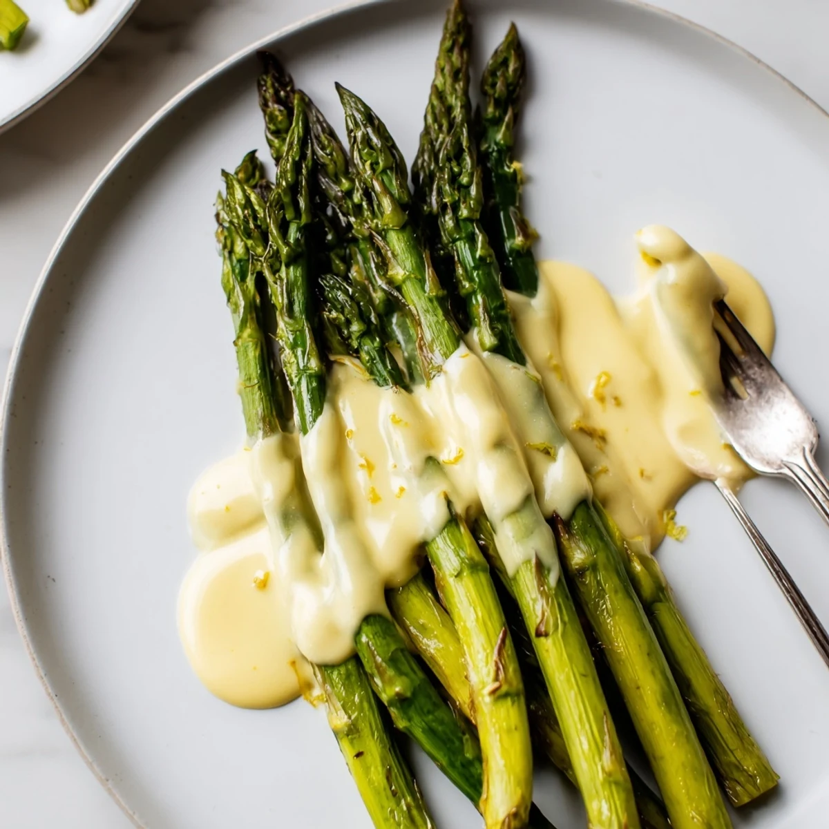 Fresh green asparagus roasted until lightly browned, drizzled with silky homemade Hollandaise Sauce on a clean white serving platter.  