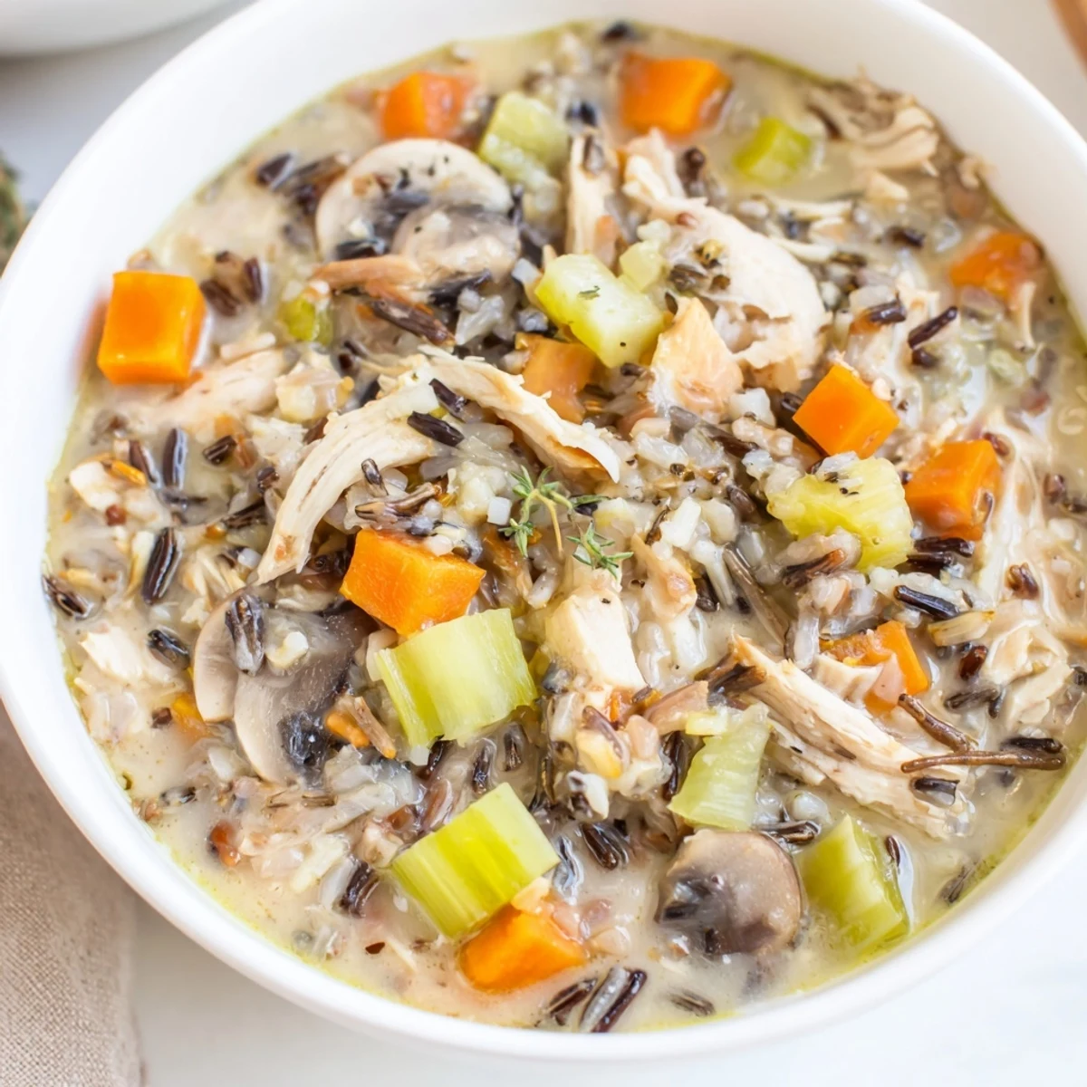 Instant Pot Chicken and Wild Rice Soup steaming in a rustic bowl, featuring tender shredded chicken, nutty wild rice, and colorful carrots and celery.