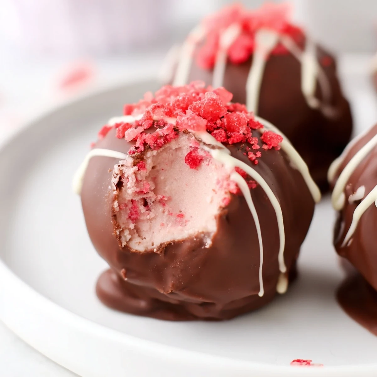 Hand holding a Chocolate Covered Strawberry Cheesecake Bite, dipped in rich dark chocolate, ready to serve at a party.