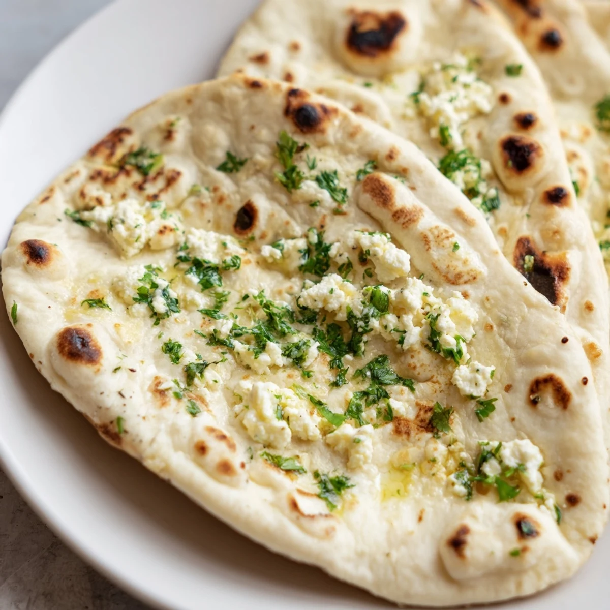 Freshly cooked Cottage Cheese Garlic Naan brushed with garlic butter beside a bowl of curry.