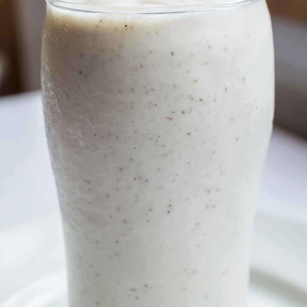 A close-up of a creamy Vanilla Bean Frappuccino topped with whipped cream and white chocolate shavings in a tall glass.