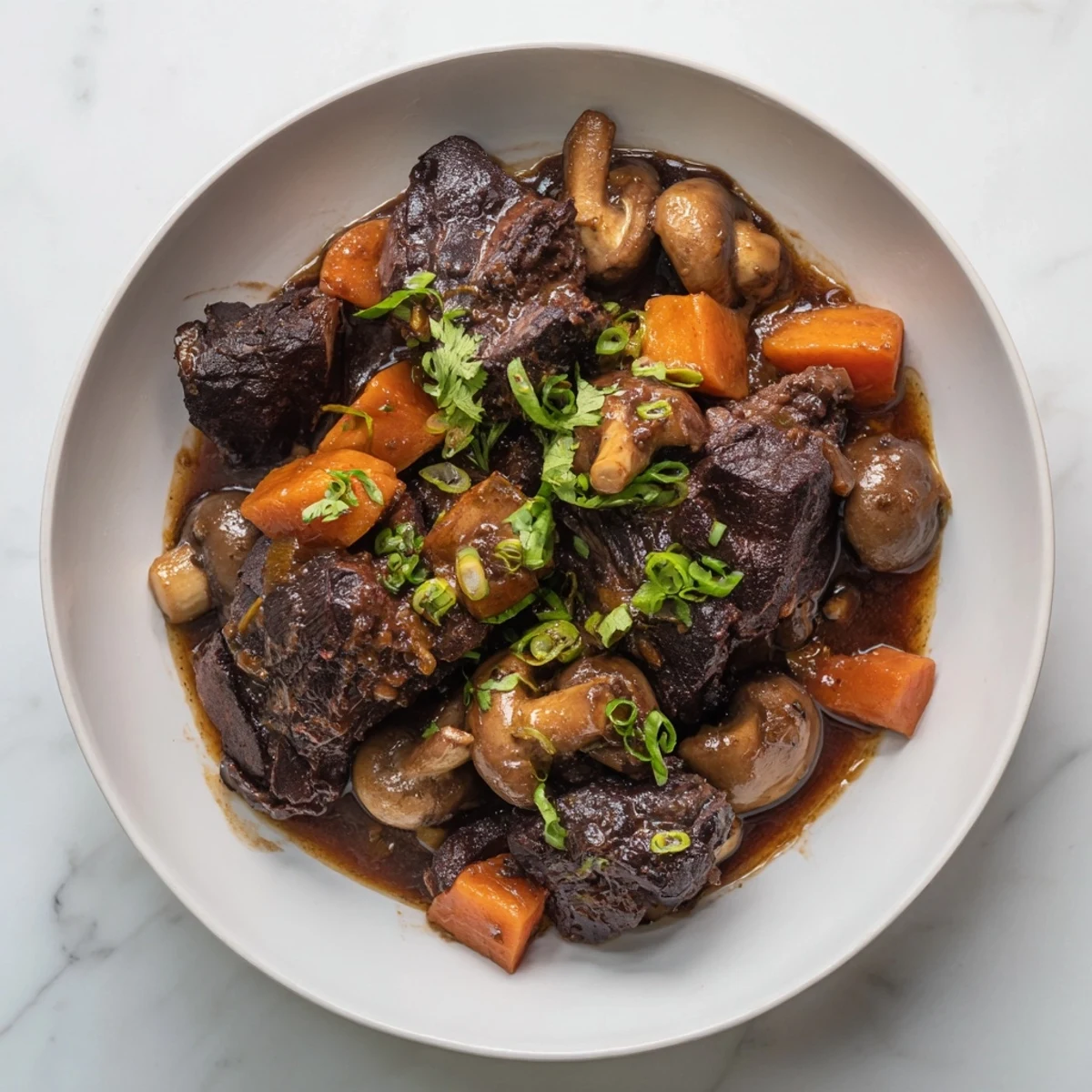 Fork-tender Asian Style Slow Cooked Beef Cheeks With Mushrooms on a white plate, surrounded by steamed jasmine rice and vibrant red chili slices.