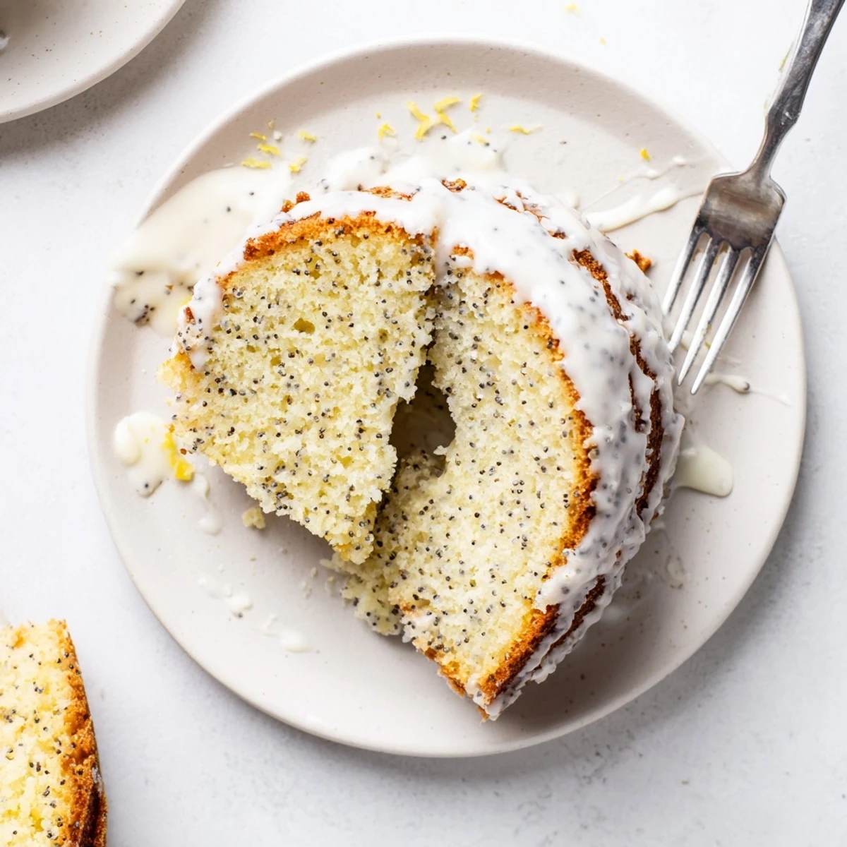A freshly baked Lemon Poppy Seed Cake in a Bundt pan, dusted with powdered sugar and lemon zest, cooling on a rustic wooden board.