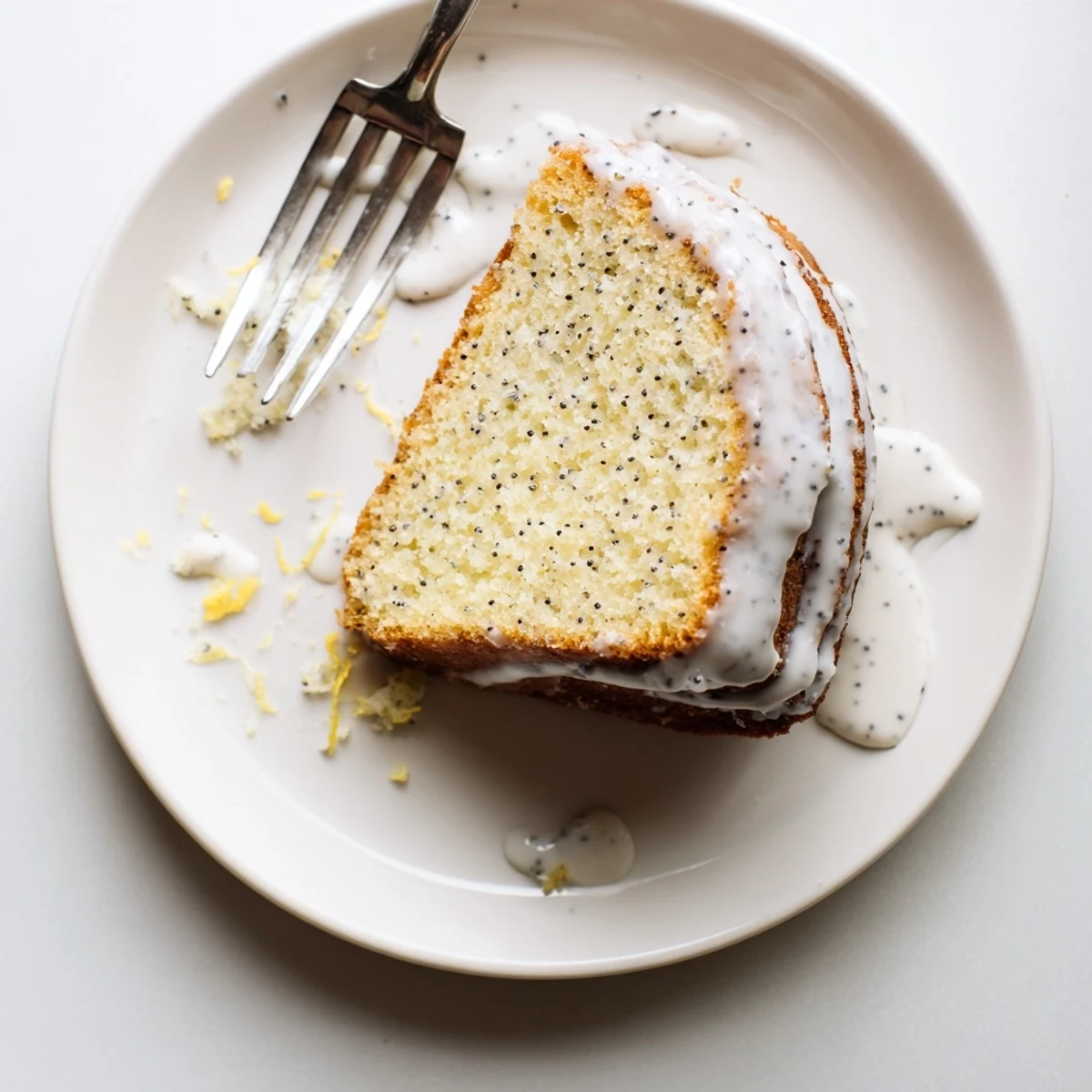 Slice of Lemon Poppy Seed Cake on a dessert plate with a cup of Earl Grey tea, highlighting the moist texture and bright citrus glaze.