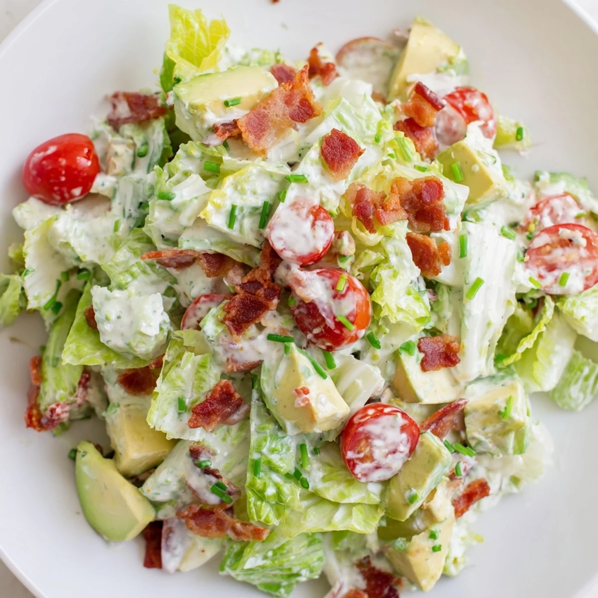 Freshly crumbled bacon and sliced red onion add savory contrast to this vibrant keto BLT salad served in a rustic white bowl.