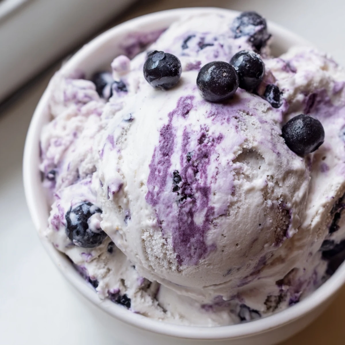 Creamy scoops of Blueberry Cottage Cheese Ice Cream served in a glass bowl with fresh blueberries.