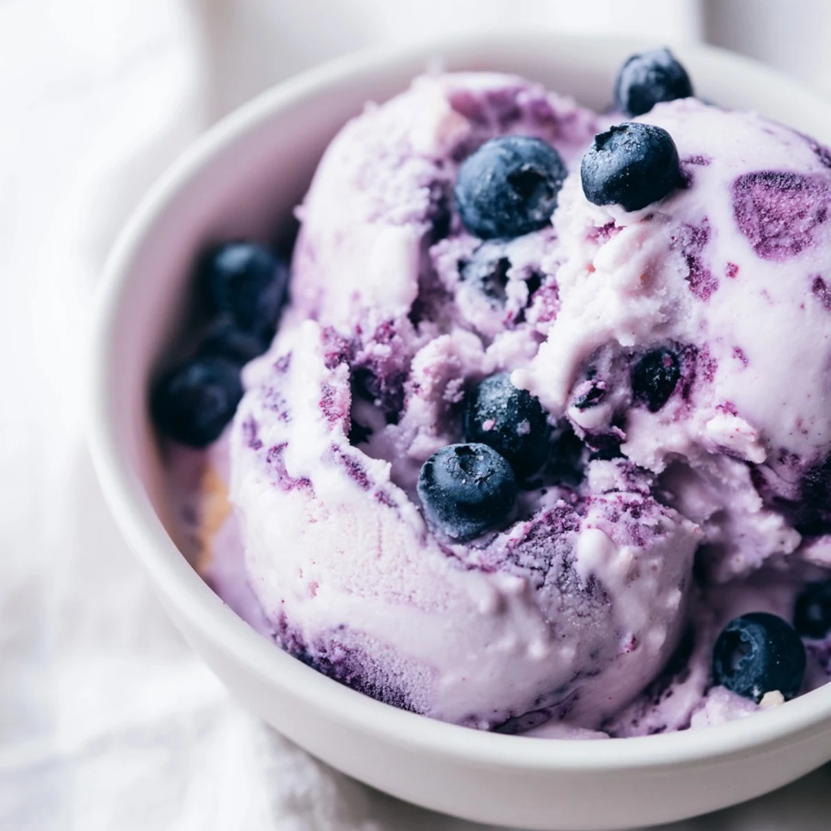 Blueberry Cottage Cheese Ice Cream in a freezer container, ready for scooping with a wooden spoon.