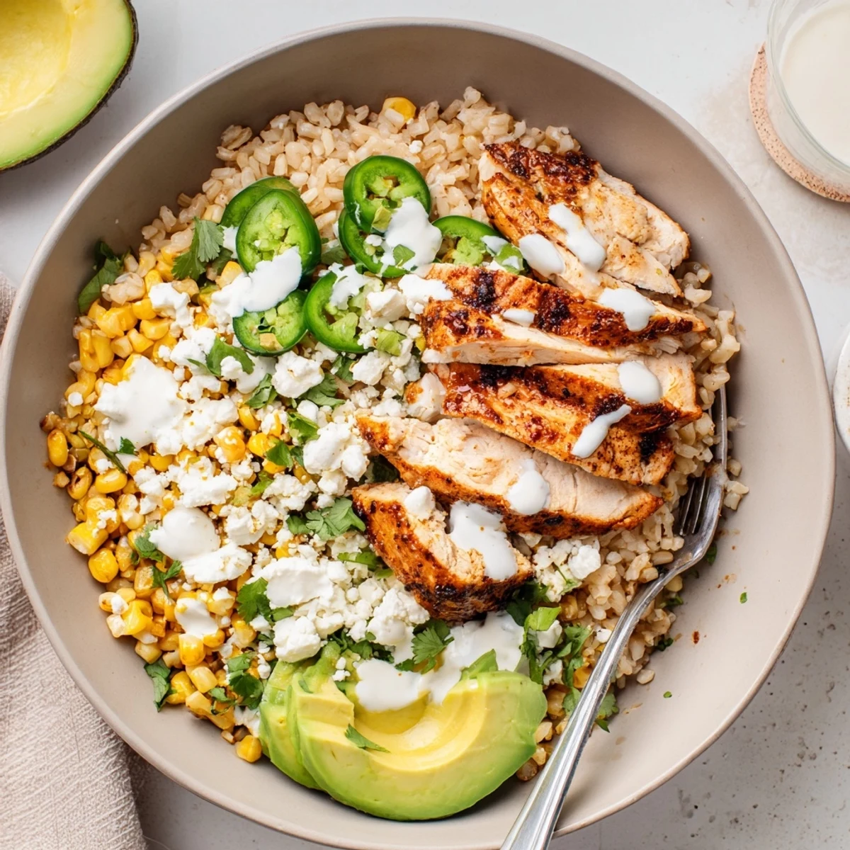Street Corn Chicken Bowl features juicy grilled chicken, sweet corn, cotija cheese, cilantro, and fresh avocado with lime wedges.
