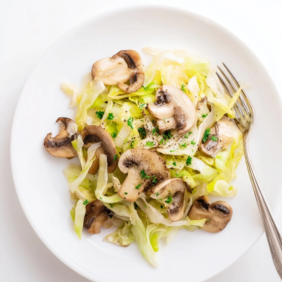 A close-up of Vegetarian Cabbage Mushroom Sauté in a skillet, with sautéed cremini mushrooms and green cabbage glistening with olive oil.