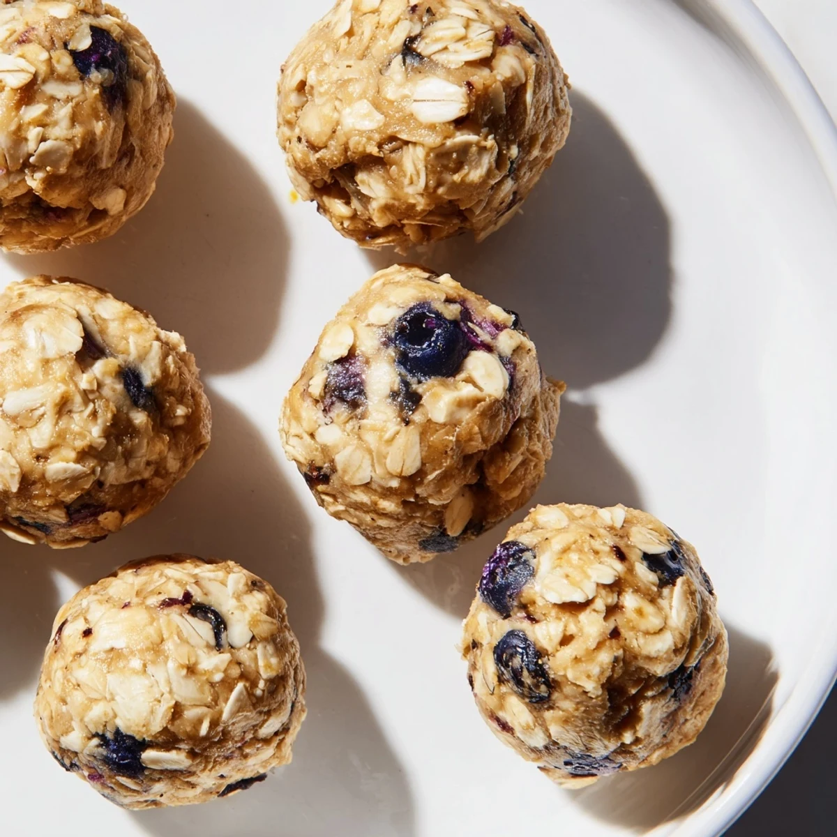 Freshly rolled Blueberry Cheesecake Protein Bites with creamy filling and fresh blueberries on a rustic wooden table.