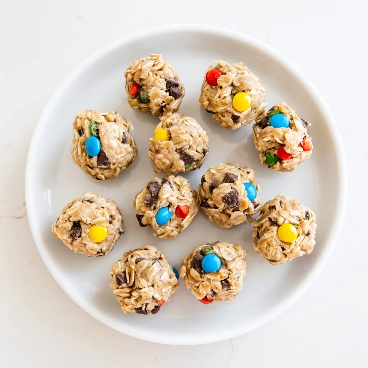 Freshly rolled Monster Cookie Protein Balls with oats, peanut butter, and colorful mini M&Ms on a chilled tray.