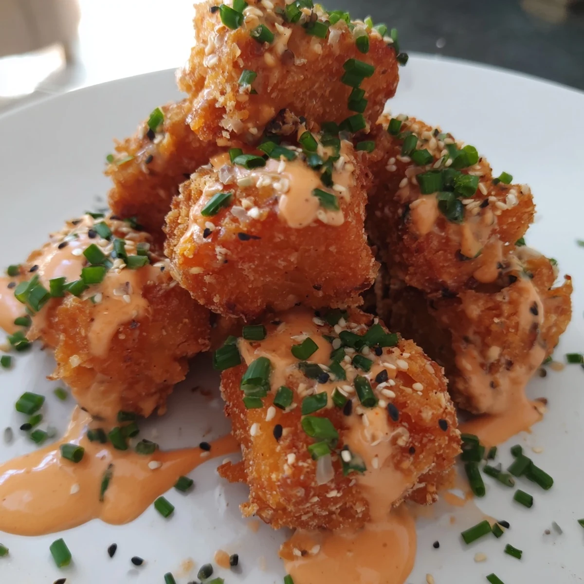 A close up of golden fried Bang Bang Salmon Bites drizzled with creamy sauce and sesame seeds.  