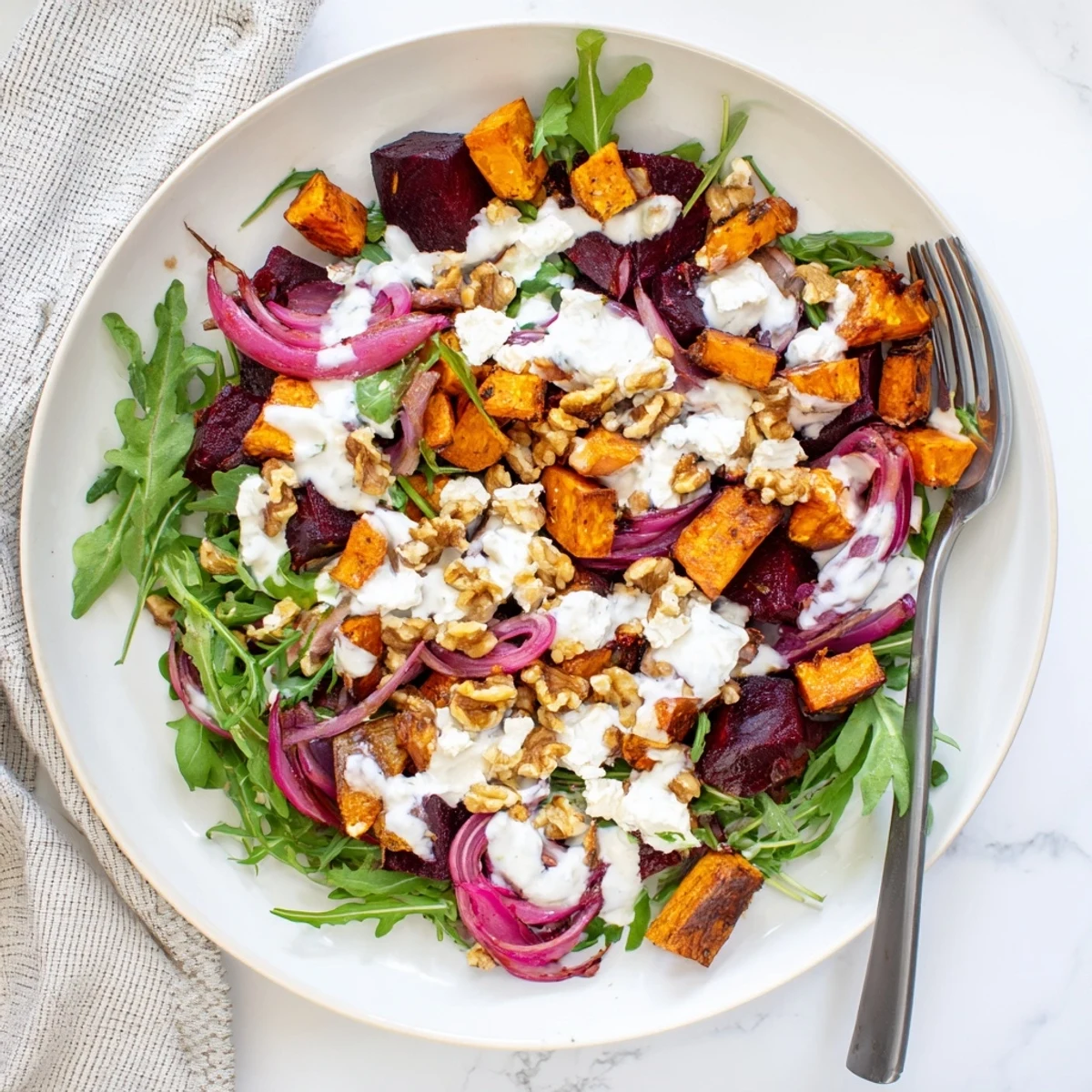 Colorful plate of roasted beet and sweet potato salad sprinkled with feta cheese and toasted nuts over mixed greens