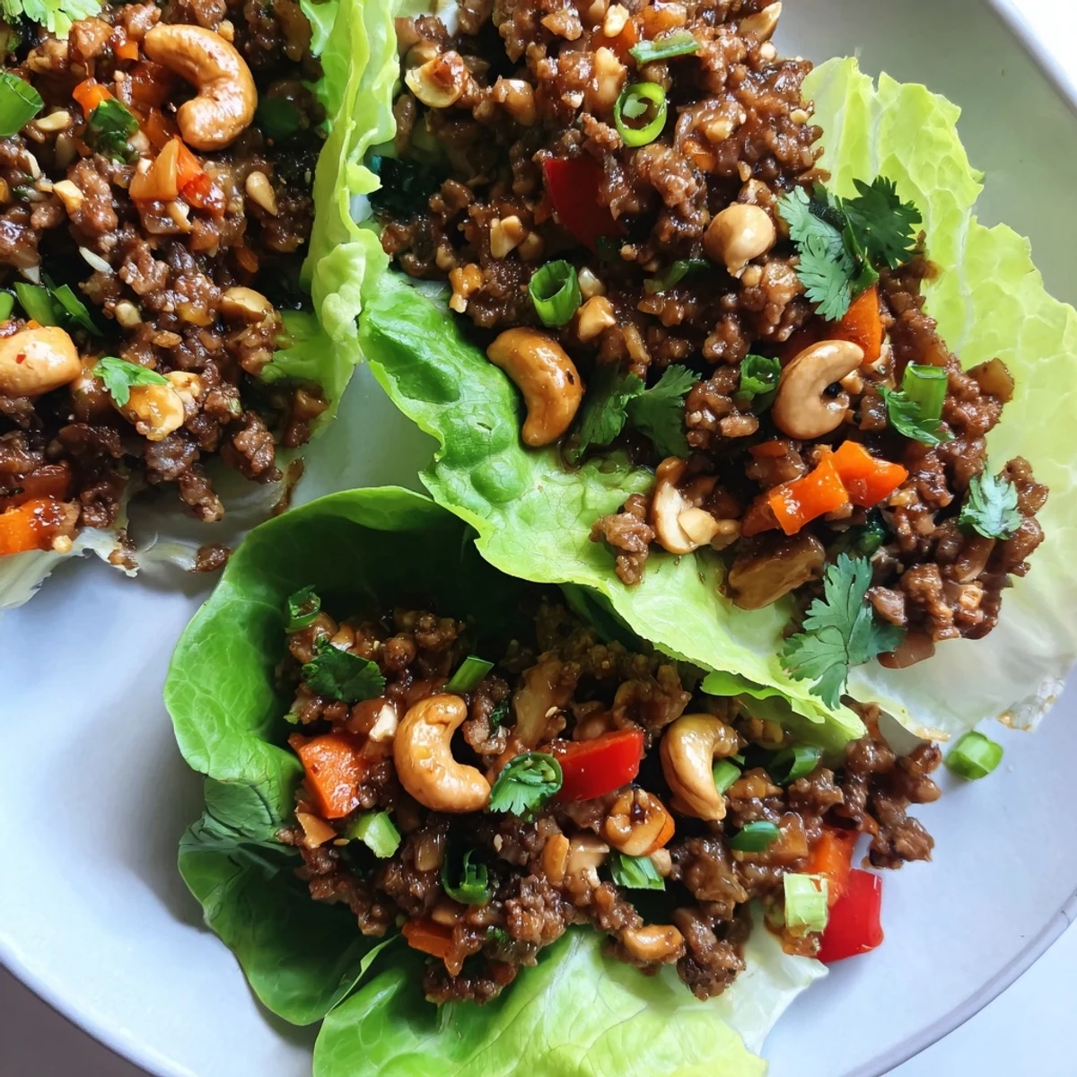 Close-up of Asian-style beef and cashew lettuce cups garnished with herbs and lime wedges