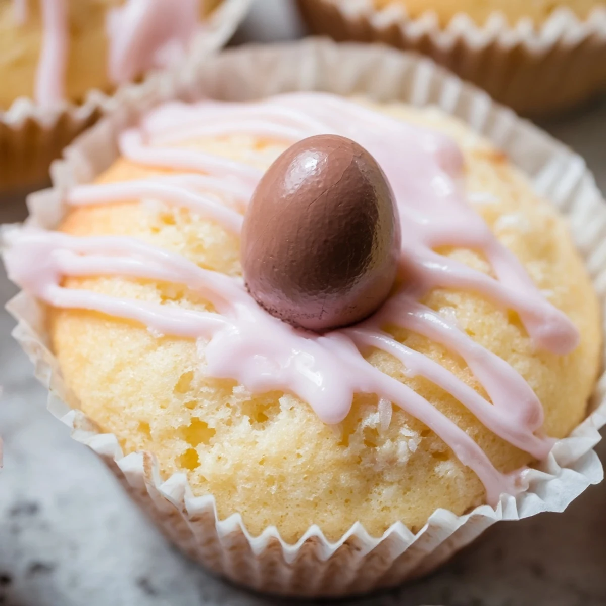 Golden mini Easter cakes topped with pastel pink icing and colorful chocolate egg decorations