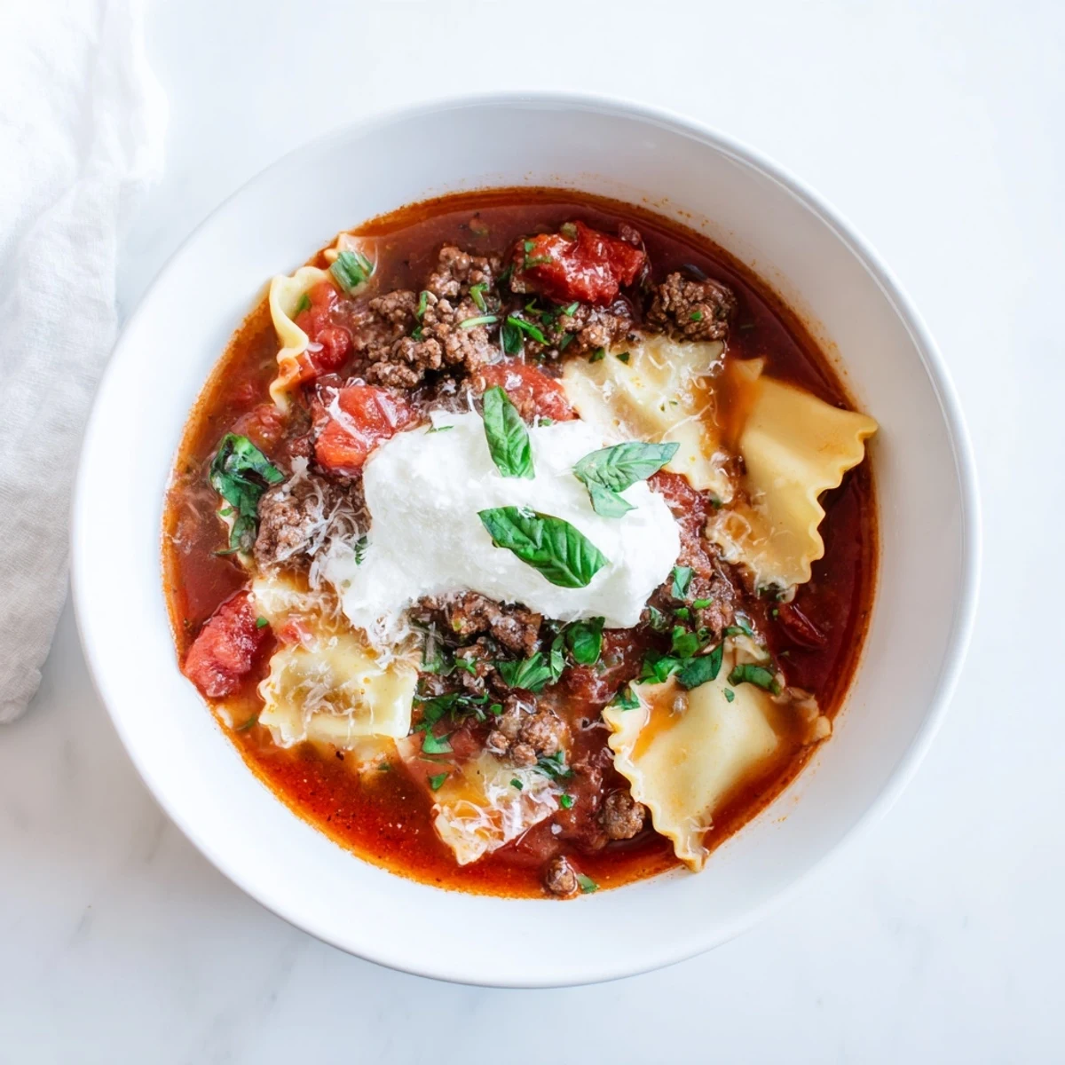 Steaming bowl of Italian lasagna soup topped with creamy ricotta dollop and fresh basil garnish