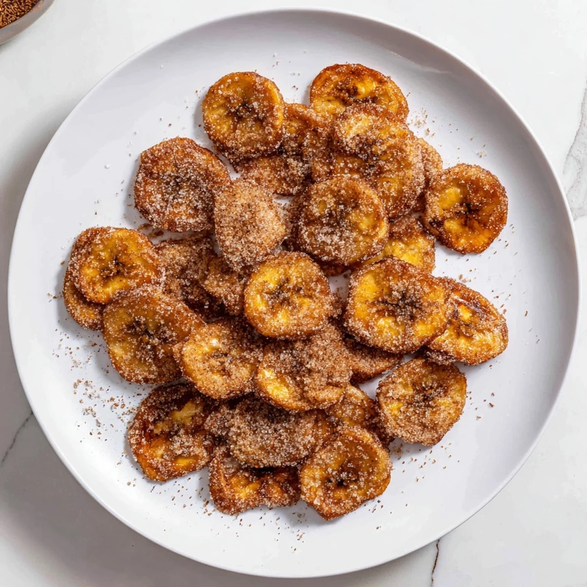 Golden cinnamon sugar air fryer banana chips arranged on a white plate with slight transparency