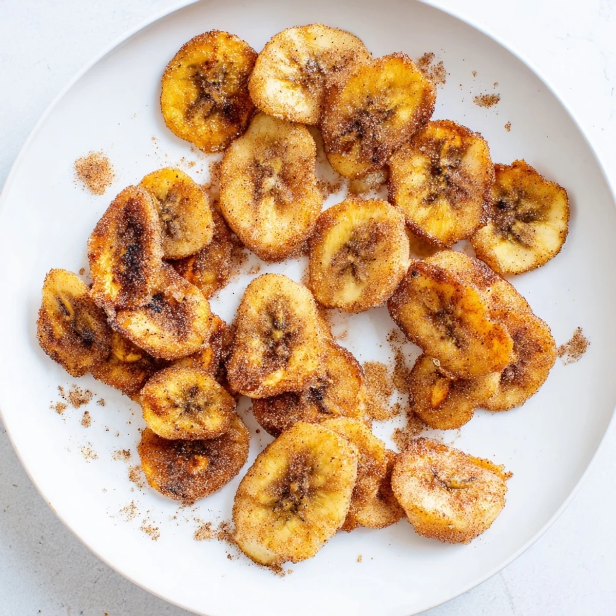 Stack of crispy cinnamon sugar banana chips freshly made in air fryer basket with golden brown edges