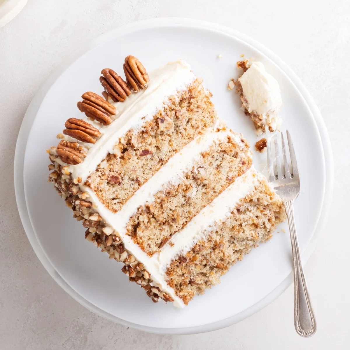 Golden butter pecan cake slice topped with creamy buttercream frosting and scattered toasted pecans