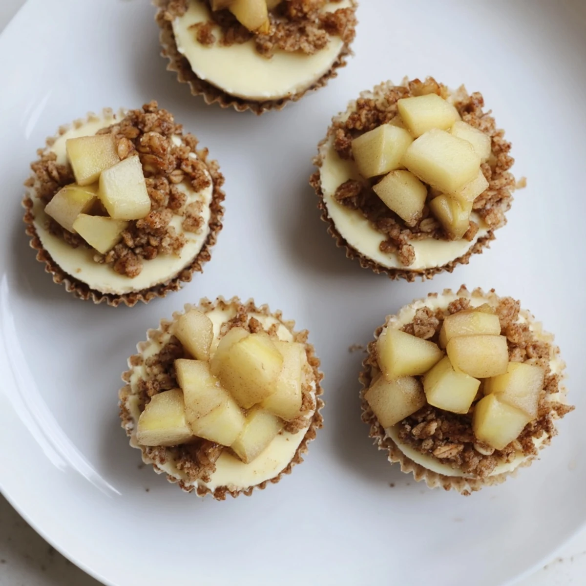 Mini cheesecakes feature graham cracker crusts topped with cinnamon apple crisp mixture