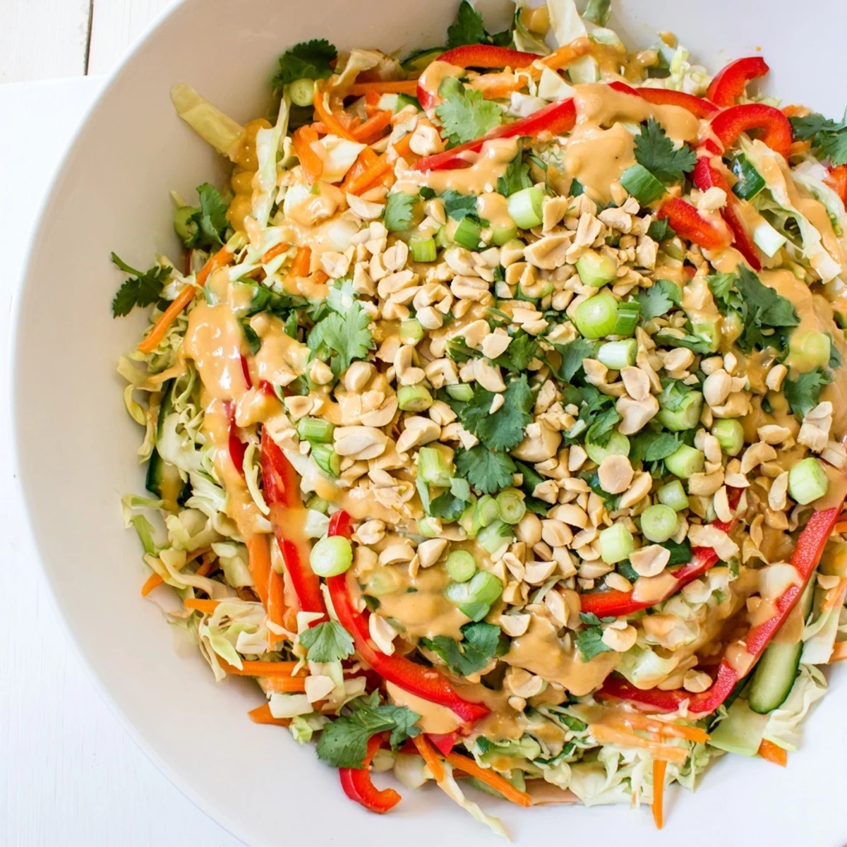 Fresh Thai salad peanut sauce drizzled over colorful shredded vegetables in a white bowl.