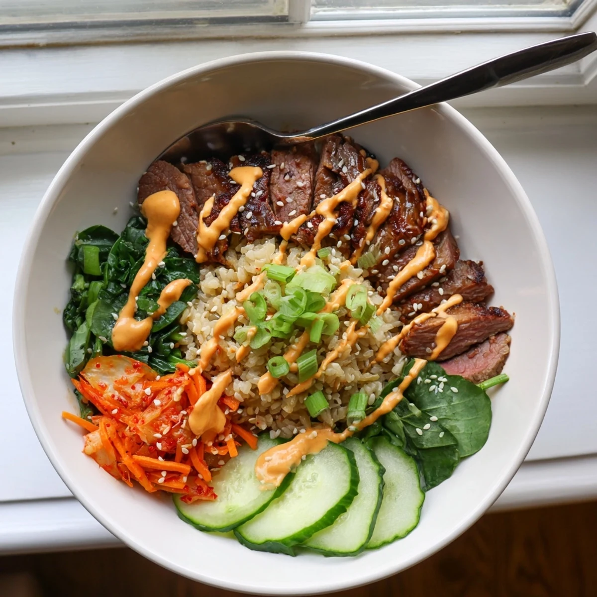 Korean BBQ steak rice bowls drizzled with creamy spicy sauce alongside crisp carrots and tangy kimchi