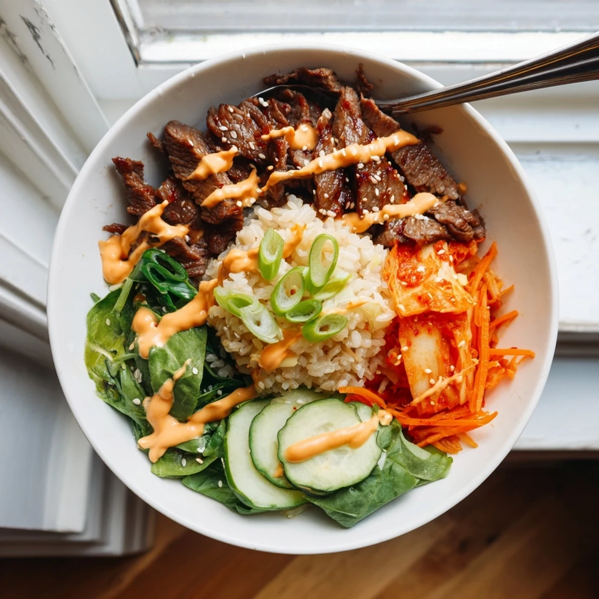 A hearty Korean BBQ steak rice bowl topped with juicy seared beef and a bold sriracha cream drizzle