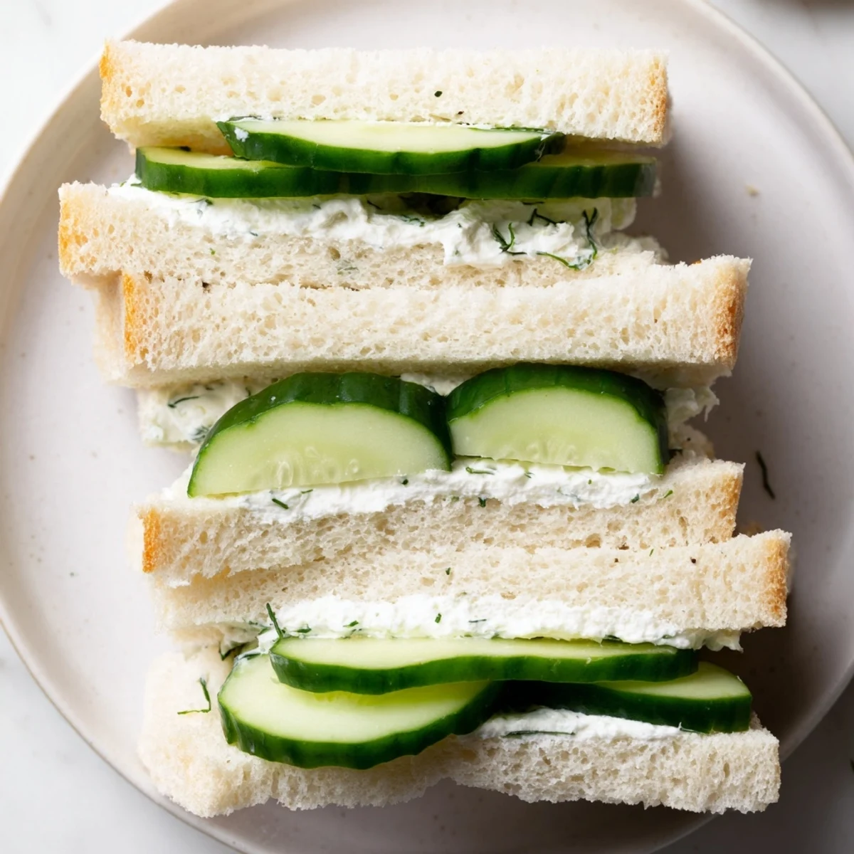 Classic Cucumber Sandwiches arranged on a china plate beside tea, thinly sliced cucumbers