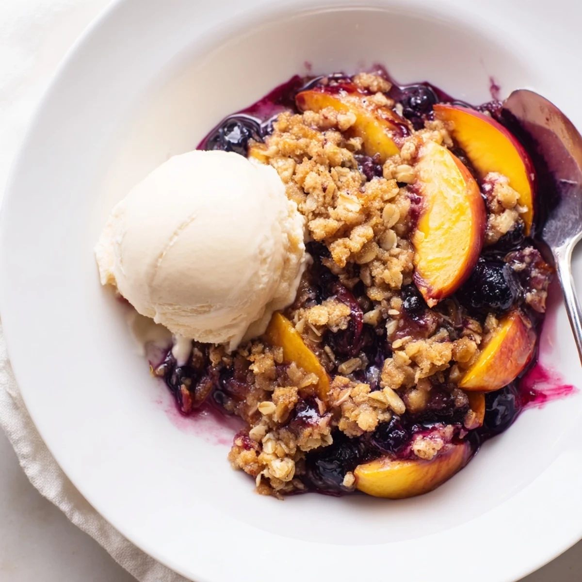 Slice of Blueberry Peach Crumble steaming on plate, oats crunch and syrupy juices