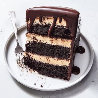 Frosted Triple Matilda Chocolate Cake slice with creamy chocolate frosting and berries on a white plate.