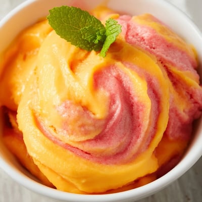 Creamy scoops of Mango Strawberry Sorbet over crushed ice with lime wedges beside it.