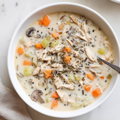 Golden creamy slow cooker chicken mushroom wild rice soup ladled into a rustic bread bowl